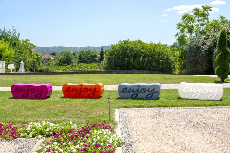 Bancs ENJOY de SLIDE colorés alignés sur une pelouse