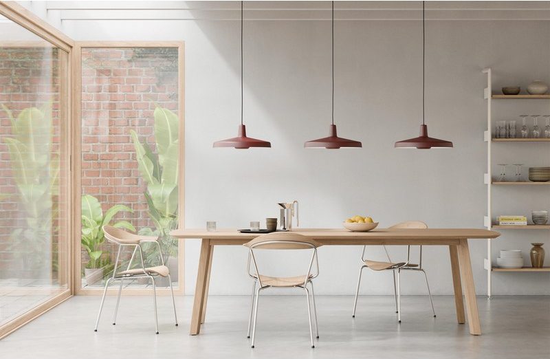 Trois suspensions rouges alignées au-dessus d'une longue table en bois dans une salle à manger lumineuse