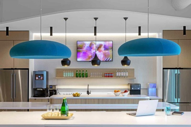 Deux grandes suspensions bleues arrondies au-dessus d'un îlot de cuisine dans une cafétéria d'entreprise